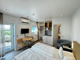 A hotel room with a bed, a desk with a chair, a small dining table with chairs, a kitchenette, and a TV mounted on the wall.