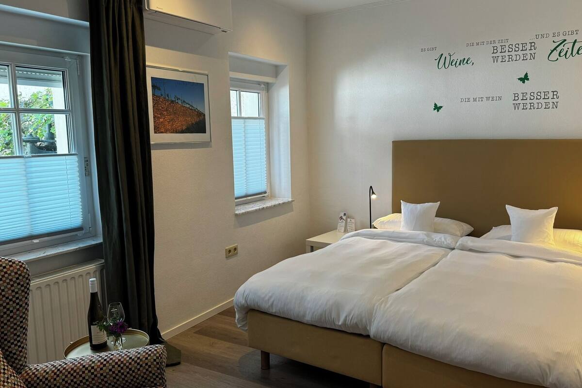 A hotel room with a large bed, a bedside table with a lamp, a chair, and a window with blinds.