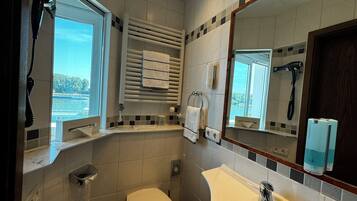 A bathroom with a toilet, sink, towel rack, and a window with a view of a body of water.