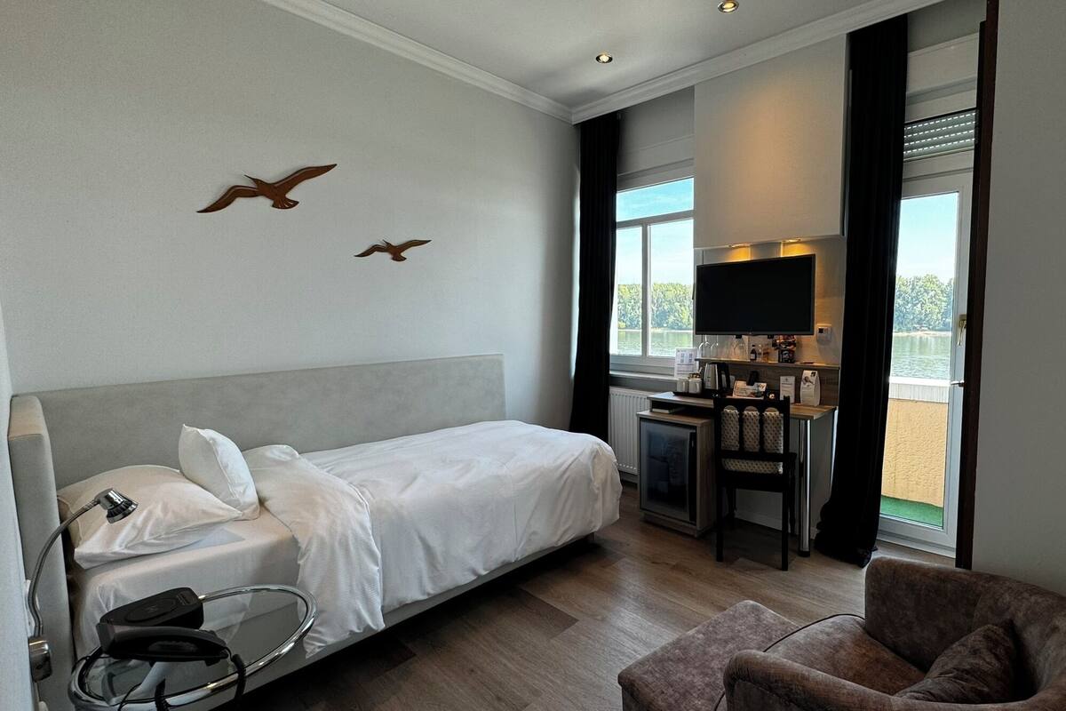 A hotel room with a bed, a desk with a computer, a chair, and a view of the outdoors.
