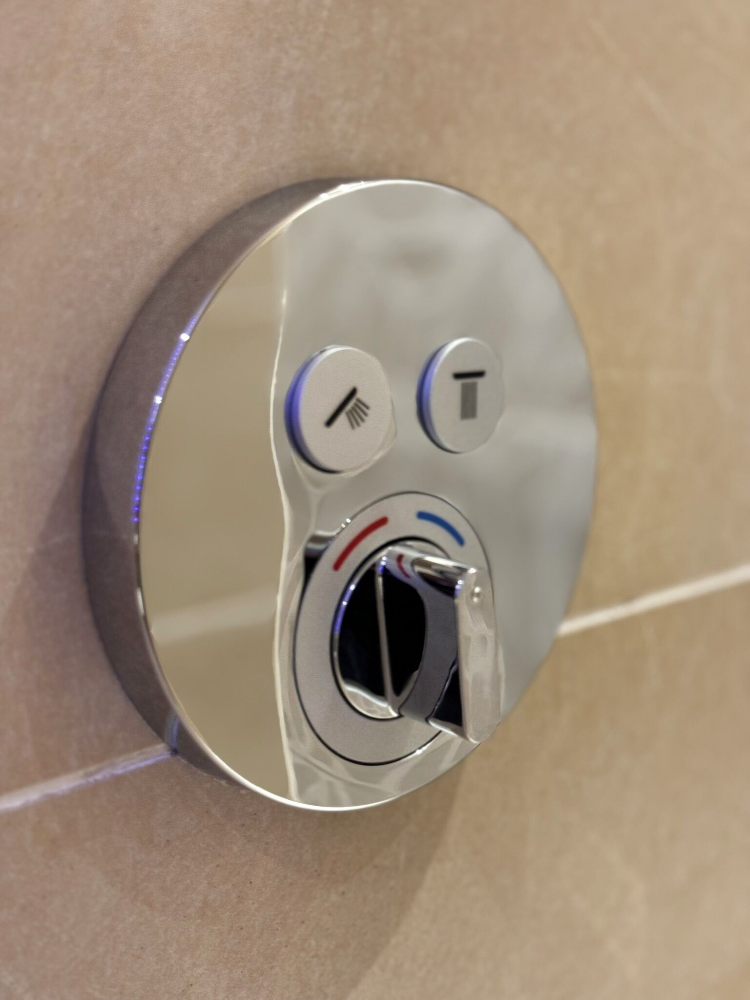 A metallic, circular object with a keyhole and two buttons, one with a cross symbol and another with a T symbol, mounted on a beige surface.