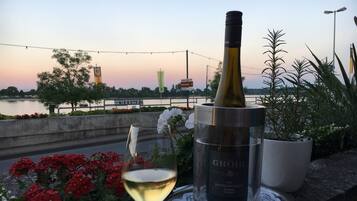 Una botella de vino, una copa de vino y una planta en maceta sobre una mesa, con vistas a un río y un puente al fondo.