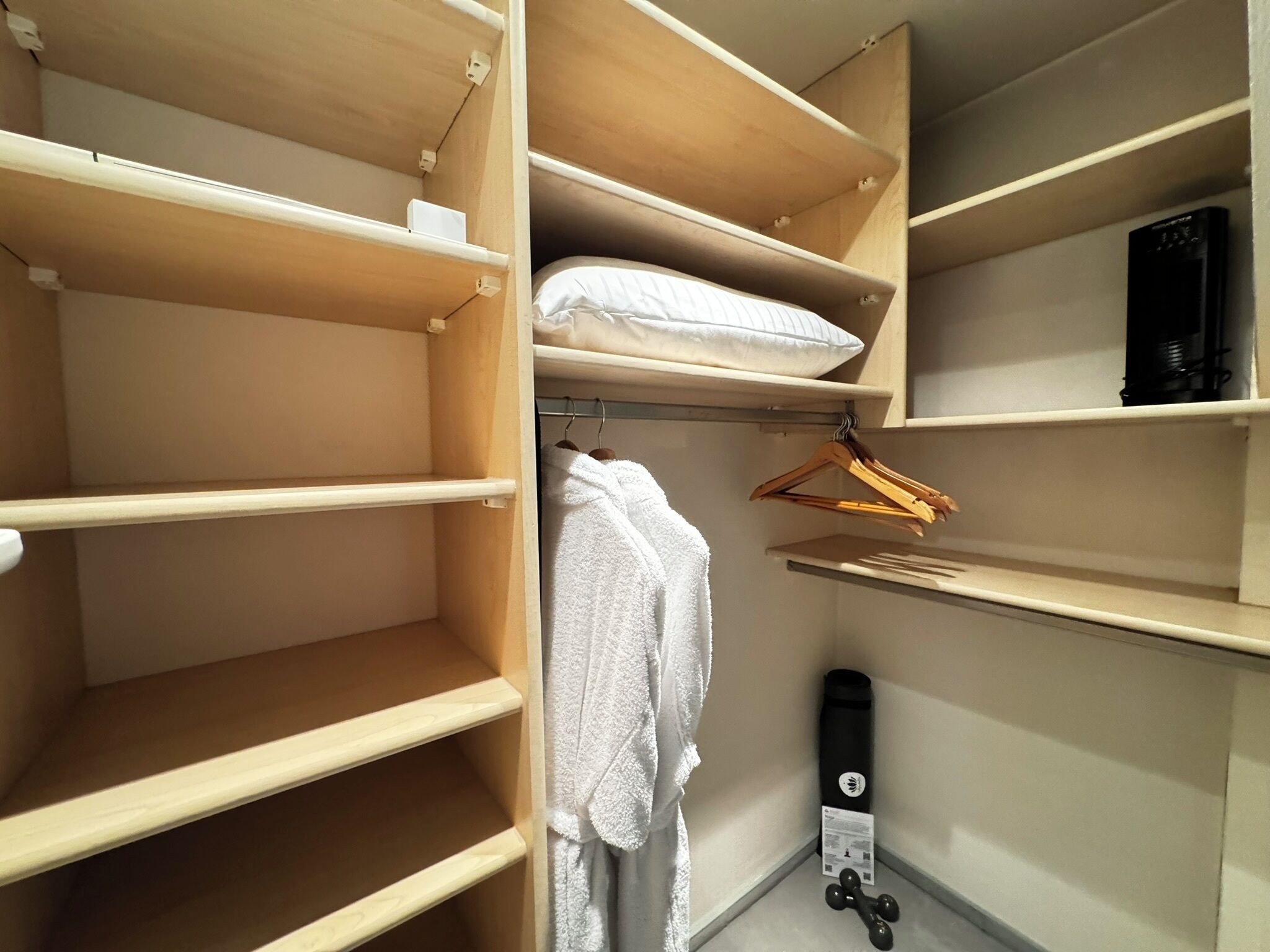 A closet with wooden shelves, a hanging rack, and a black exercise equipment.