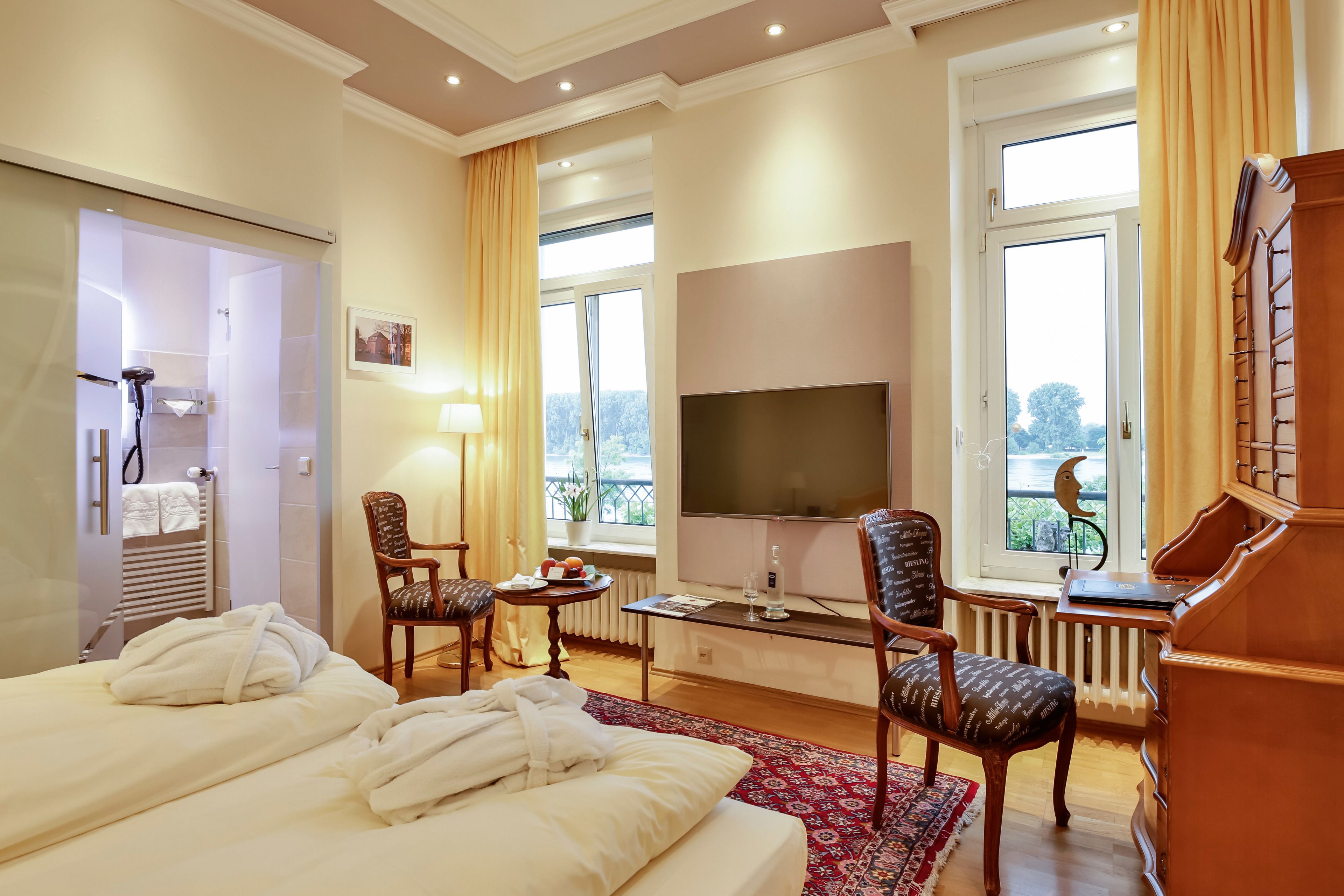 A hotel room with a bed, two chairs, a TV, a small table with a lamp, and a view of the outdoors.