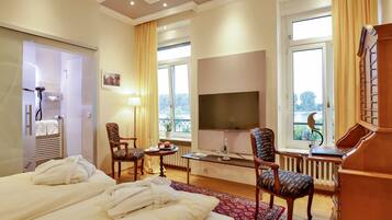 A hotel room with a bed, two chairs, a TV, a small table with a lamp, and a view of the outdoors.