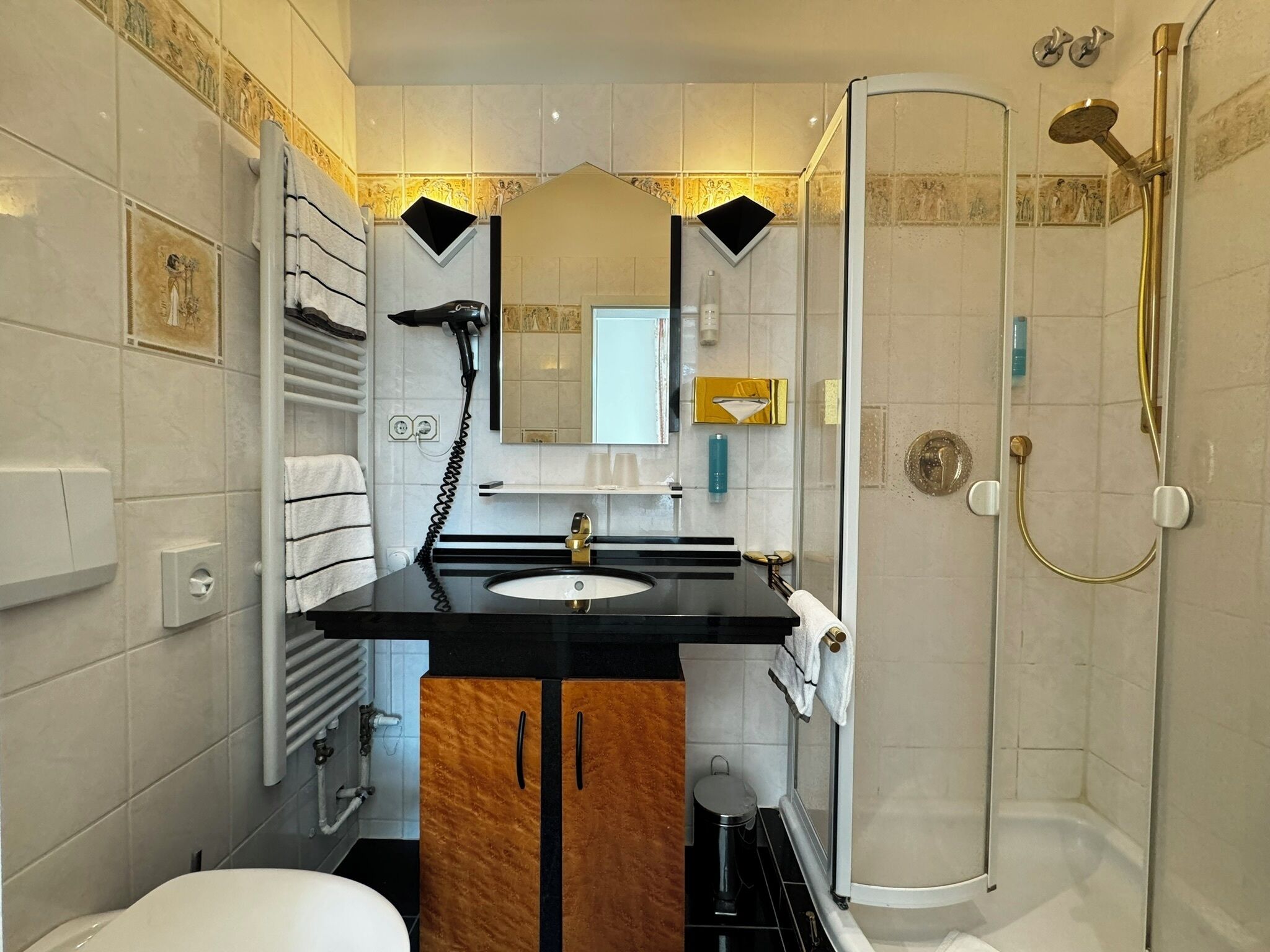 A modern bathroom with a black countertop sink, a mirror, a towel rack, a shower with a gold showerhead, and a toilet.