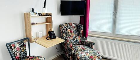 Una habitación con un escritorio de madera, una silla, un televisor y un radiador.