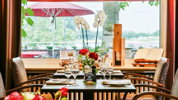 Una mesa de restaurante dispuesta con copas de vino, un menú y un florero con flores.