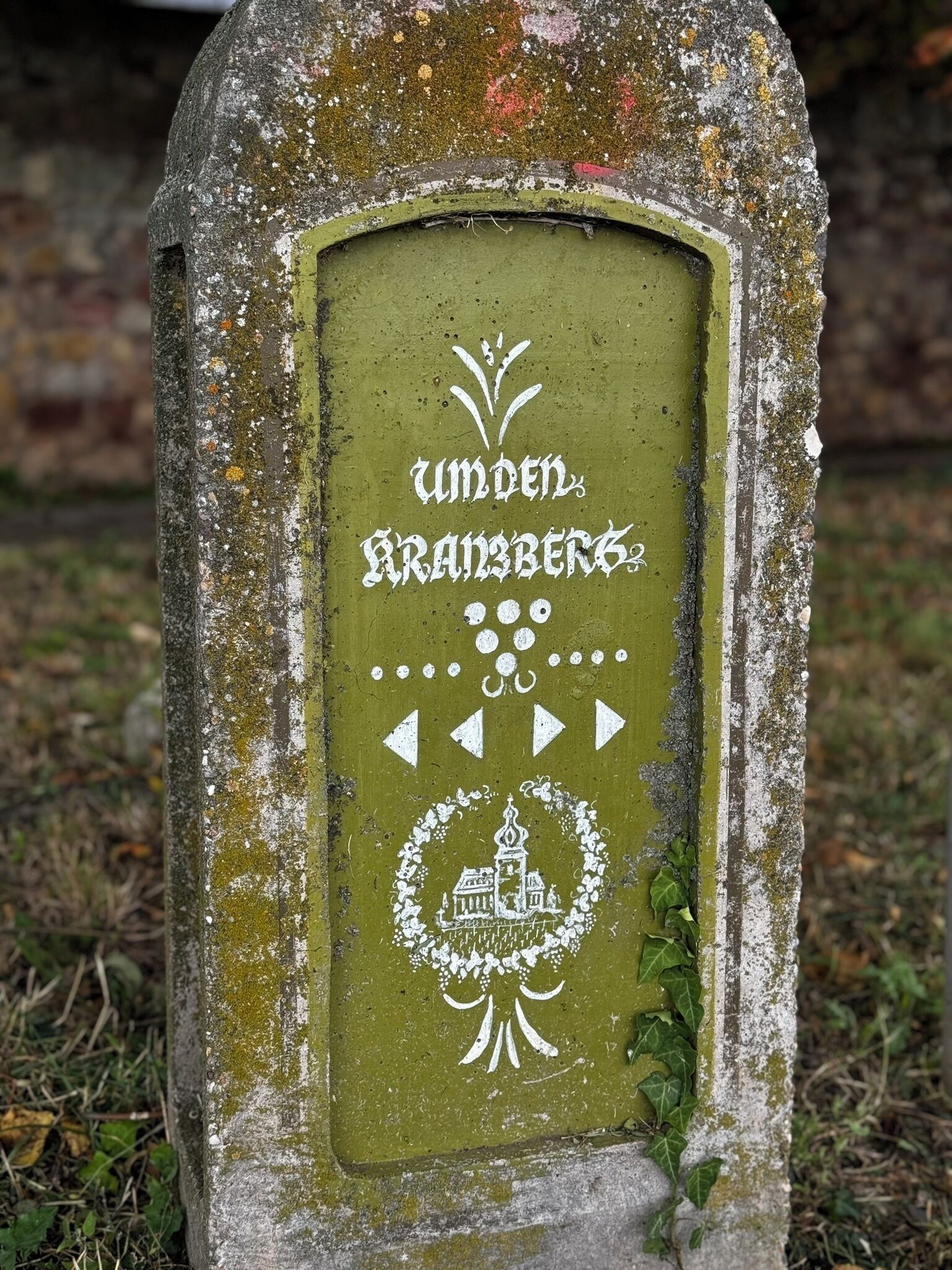 A weathered gravestone with inscriptions and symbols, surrounded by grass and moss.