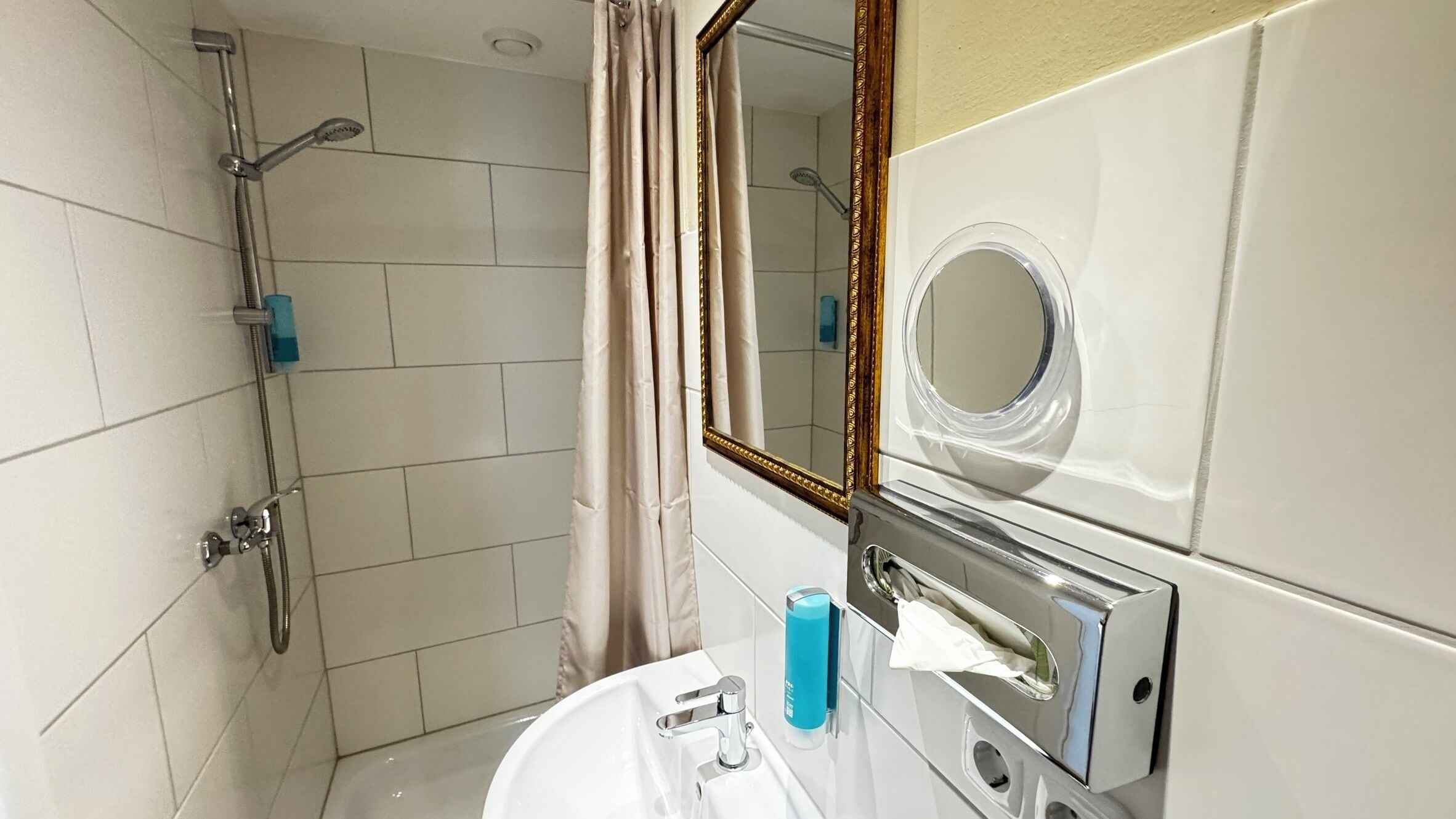 Une salle de bain équipée d’une douche, d’un lavabo, d’un miroir et d’un distributeur de serviettes.