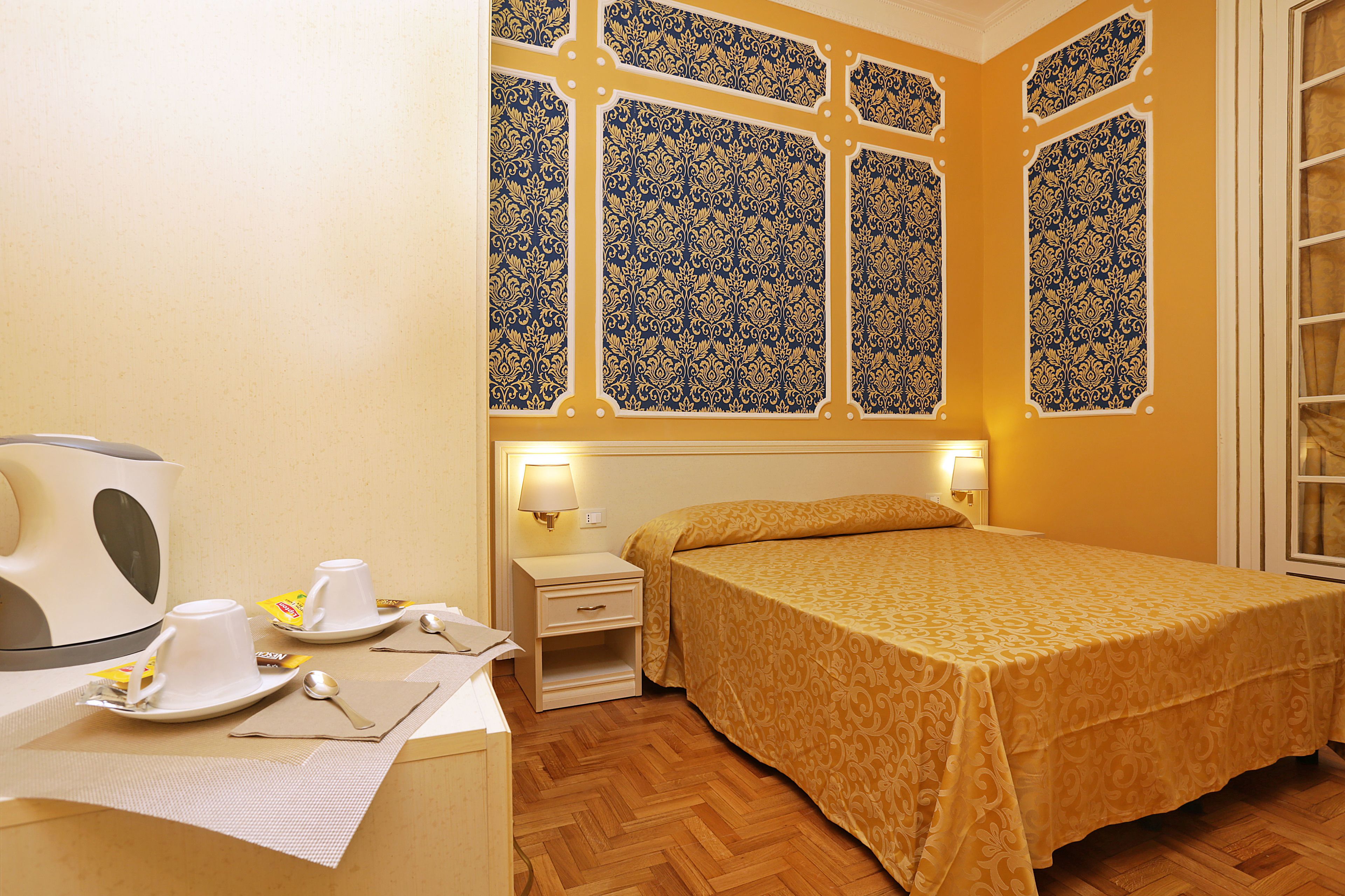 A hotel room with a bed, bedside table, lamp, and a window with decorative panes.