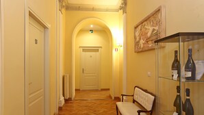 A hotel hallway with a wooden floor, a bench, a glass display case with bottles, and a door marked with the number 19. - DG Prestige Room (Rome)