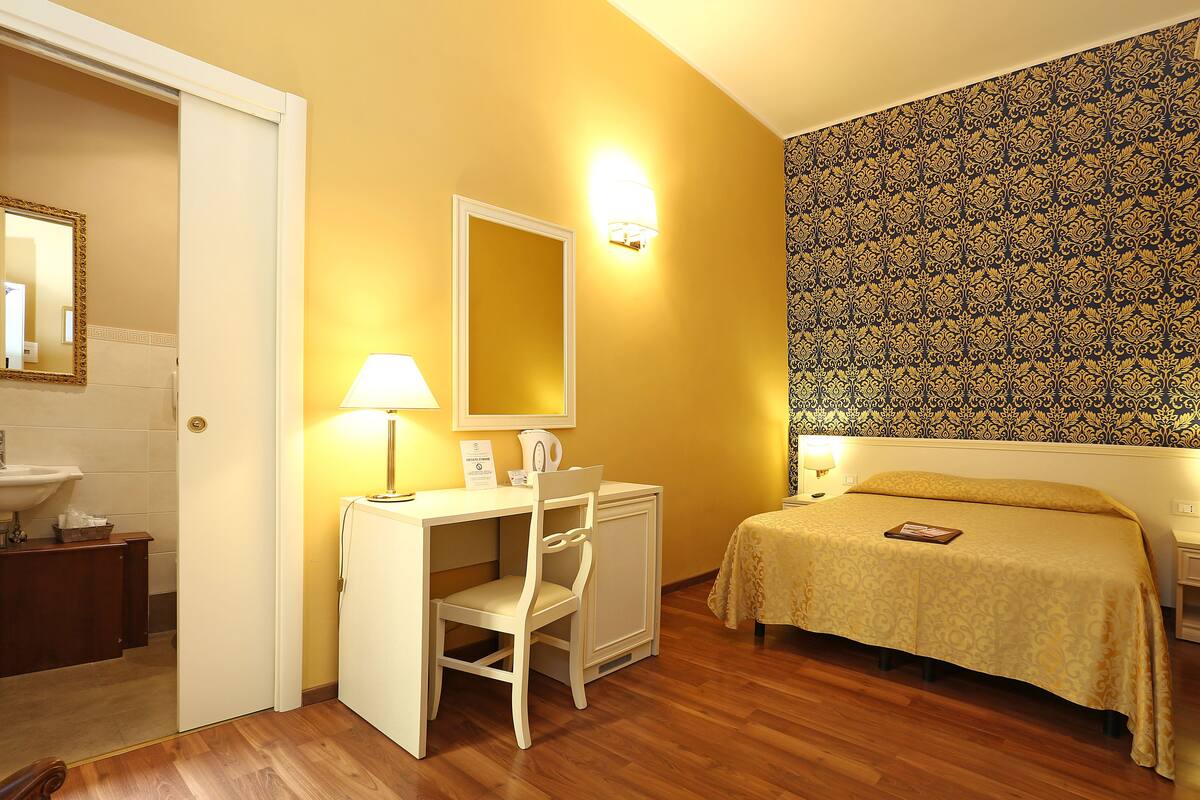A hotel room with a desk, chair, bed, and a bathroom with a sink.