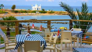 An outdoor dining area with tables and chairs, overlooking a beach and the sea. - Myroandrou Beach Apartments (Paralimni)