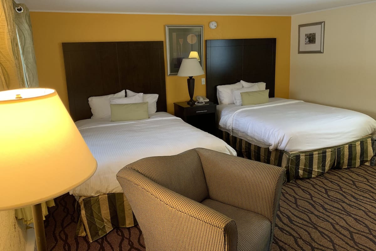 A hotel room with two beds, a nightstand with a lamp, a chair, and a framed picture on the wall.