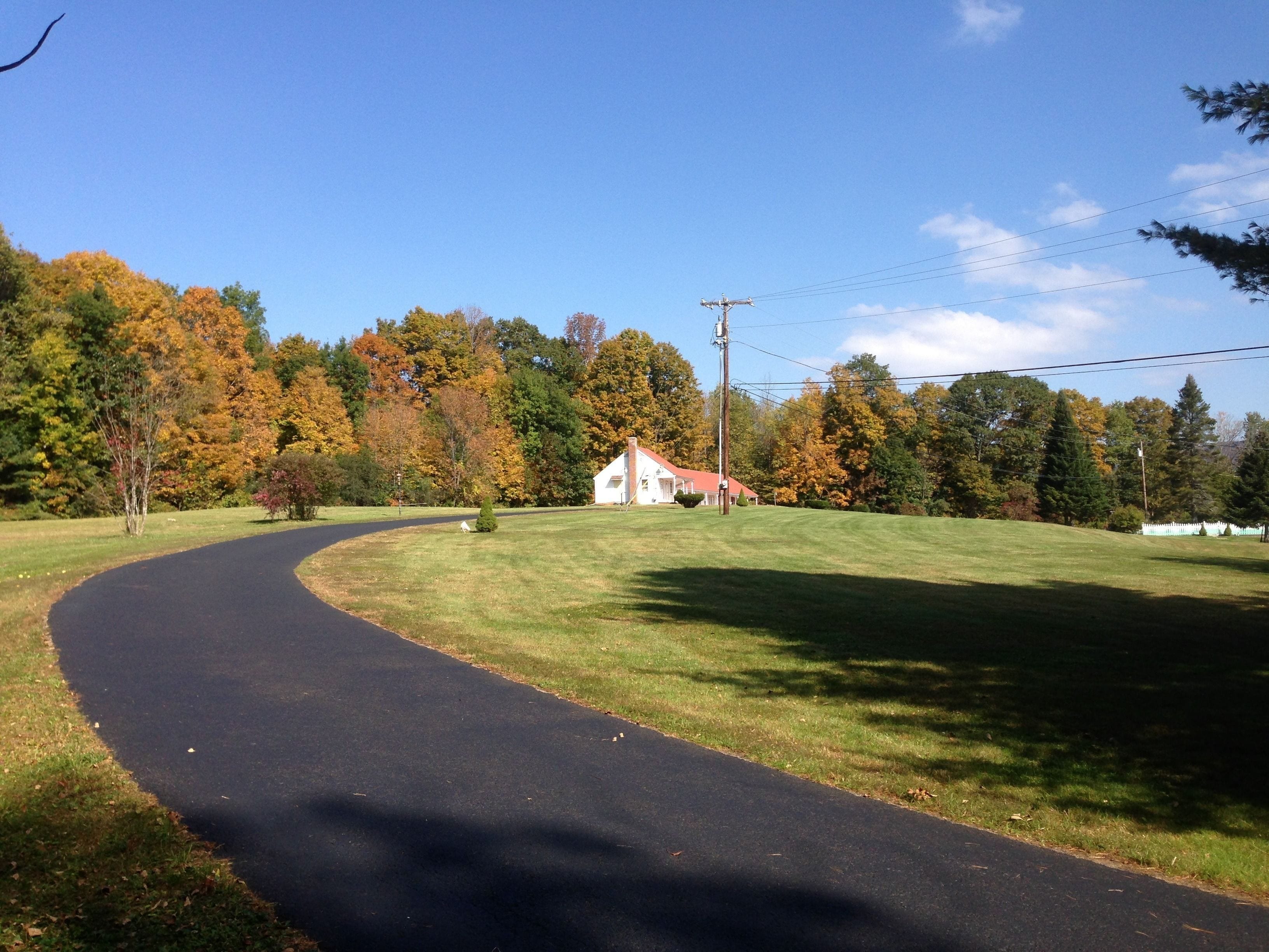 A rural road curving through a grassy area with a white house in the distance.