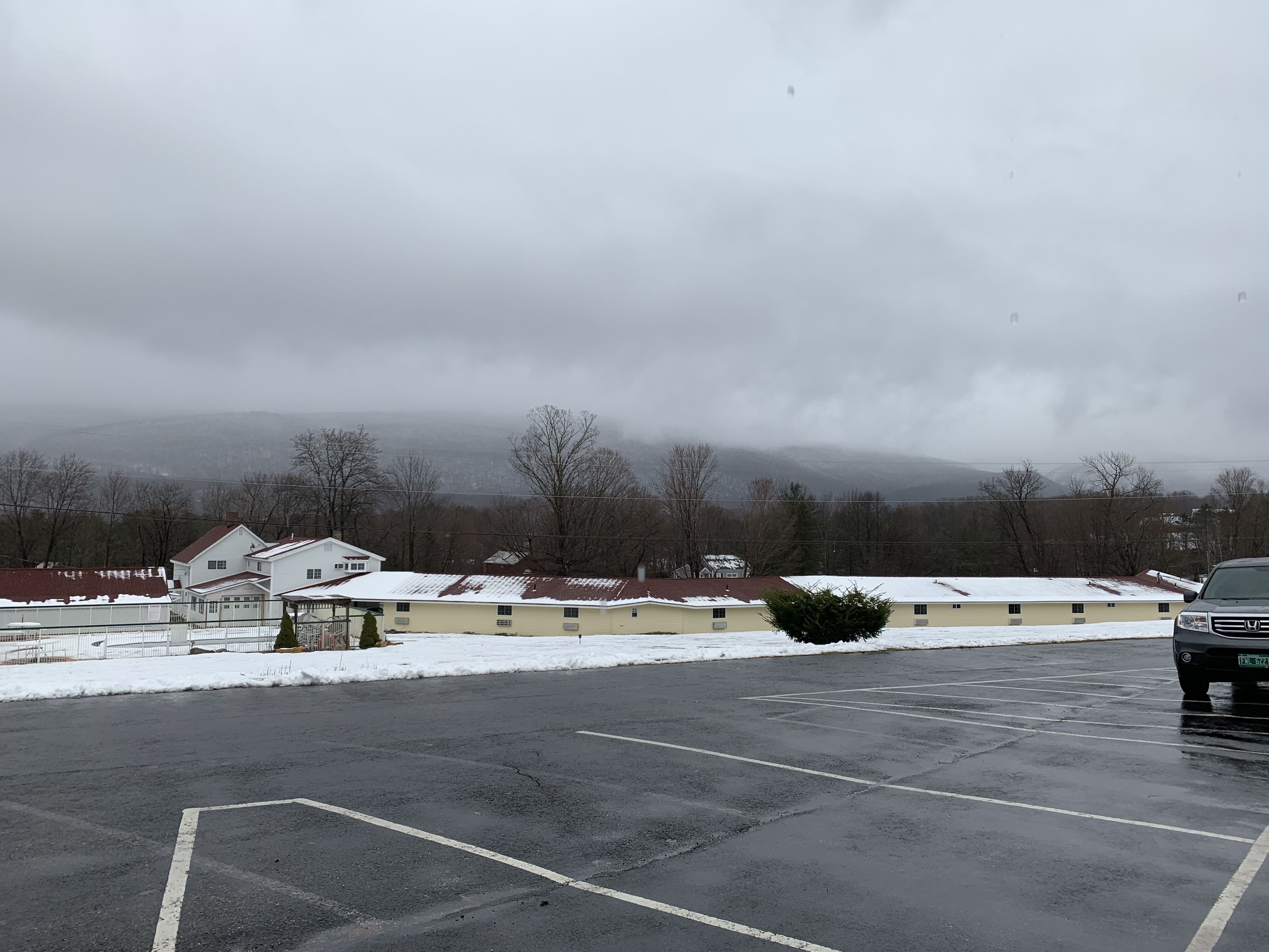 A parking lot with a Honda SUV, buildings with snow-covered roofs, and a mountainous backdrop.