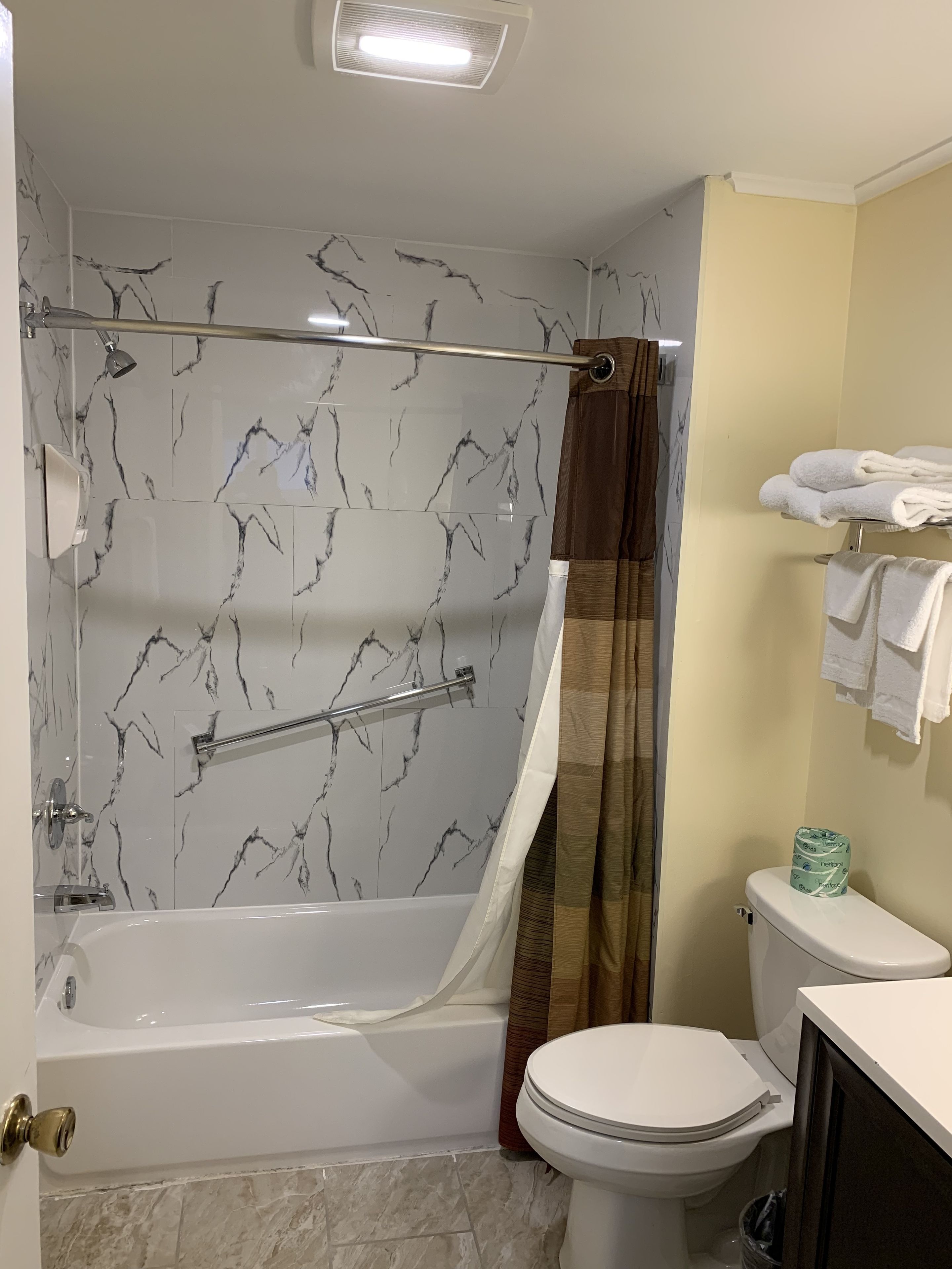 A bathroom with a bathtub, shower, toilet, and a towel rack.
