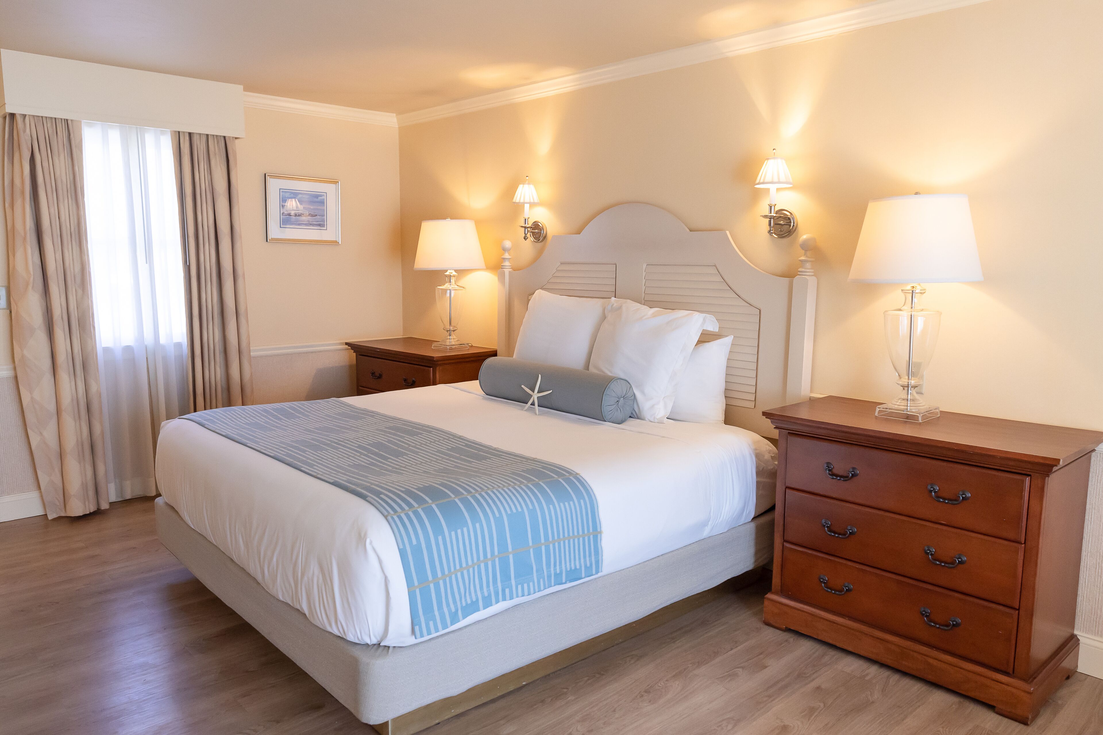 A neatly made bed with a blue and white striped blanket, two bedside tables with lamps, and a wooden nightstand with drawers.