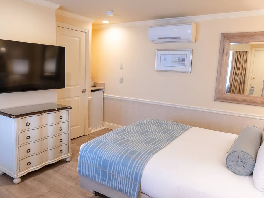 A bedroom with a bed, a dresser, a TV, and a mirror.
