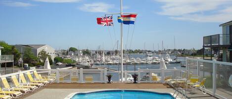A pool area with lounge chairs and a view of a marina with boats and flags.