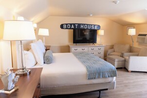 Quarto com cama, luminárias de cabeceira, televisão, cômoda, cadeira e uma placa que diz 'Boat House'.