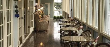 A corridor with wooden flooring, wicker furniture, and large windows.