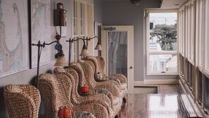 A row of wicker chairs with cushions, a map on the wall, and a view of the outside through a window. - Anchor In Distinctive Waterfront Lodging (Hyannis)