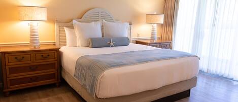 Una cama grande con cabecera, dos mesitas de noche con lámparas, un aparador de madera y un ventanal con cortinas.