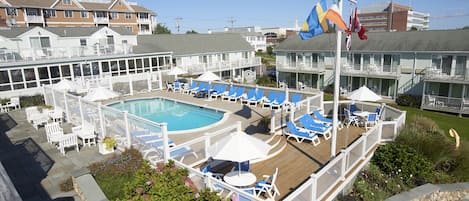 A pool area with lounge chairs and umbrellas, surrounded by a wooden deck and a white fence.
