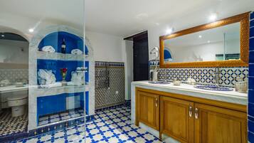Une salle de bain avec un sol à carreaux bleus et blancs, un lavabo en marbre, des meubles en bois et un grand miroir doté d’un cadre décoratif.
