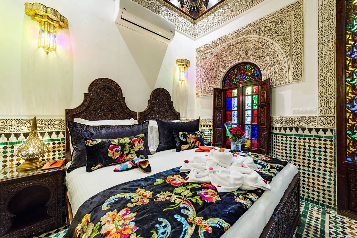 A room with a large bed, ornate headboard, decorative wall sconces, and a stained glass window.