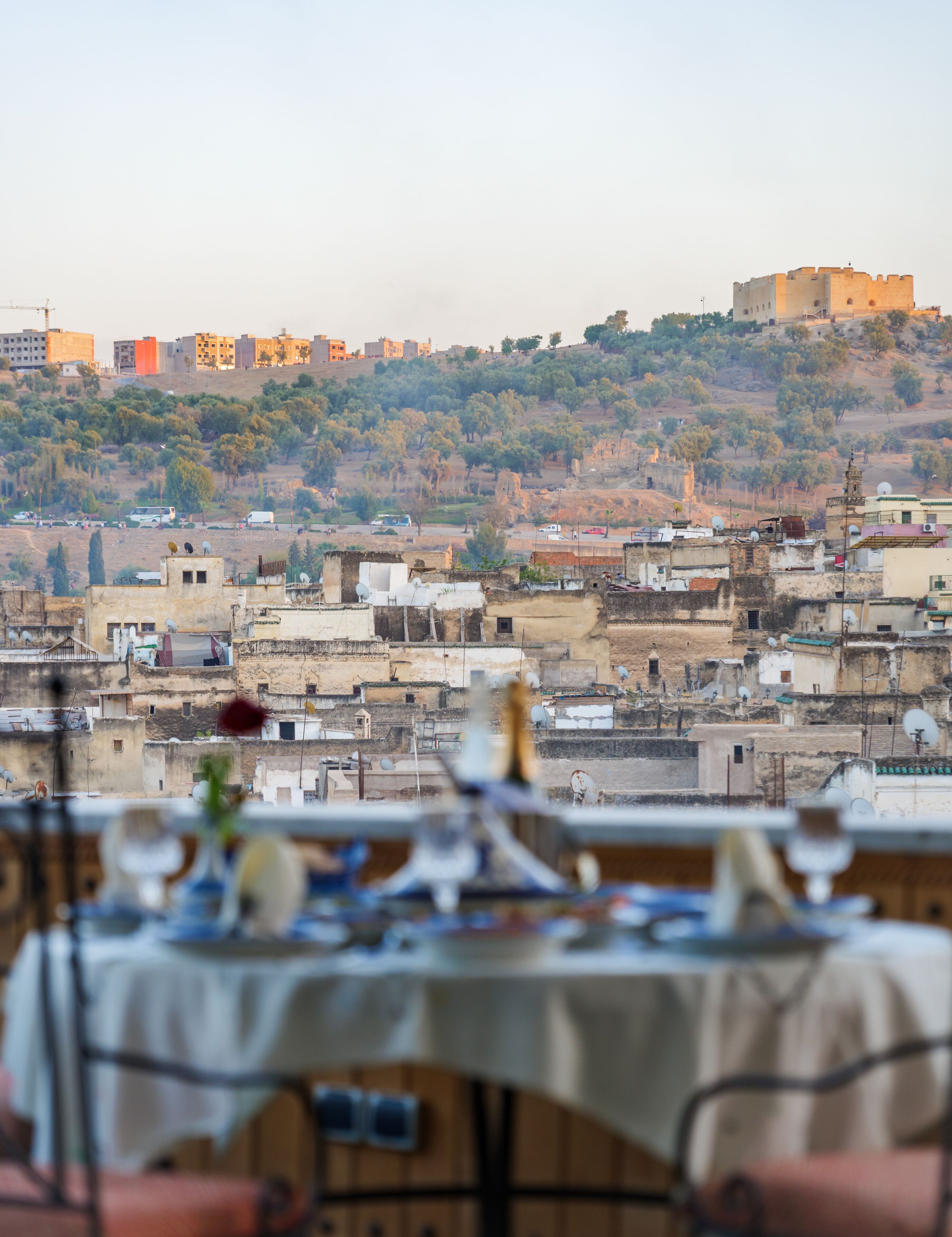 Vista de un paisaje urbano con una mesa lista para comer, con vistas a edificios y una colina con árboles.