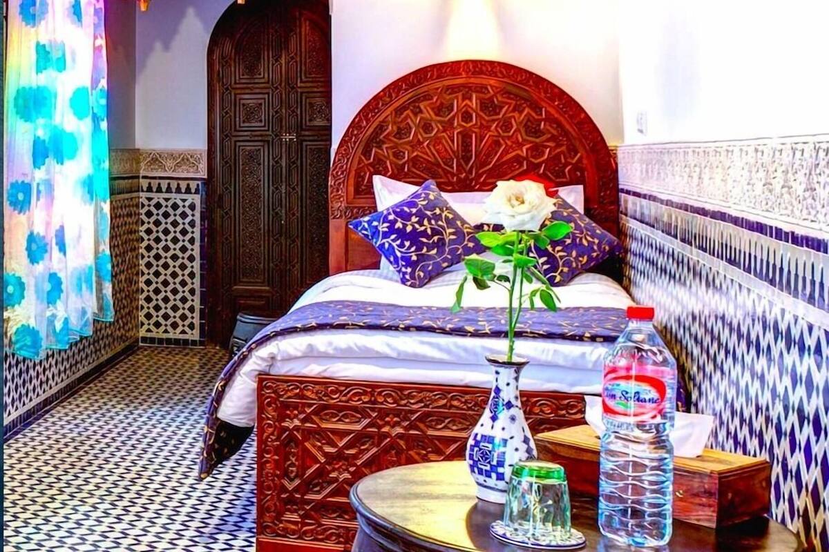 A room with a bed, a vase with a flower, a bottle, and a small table.