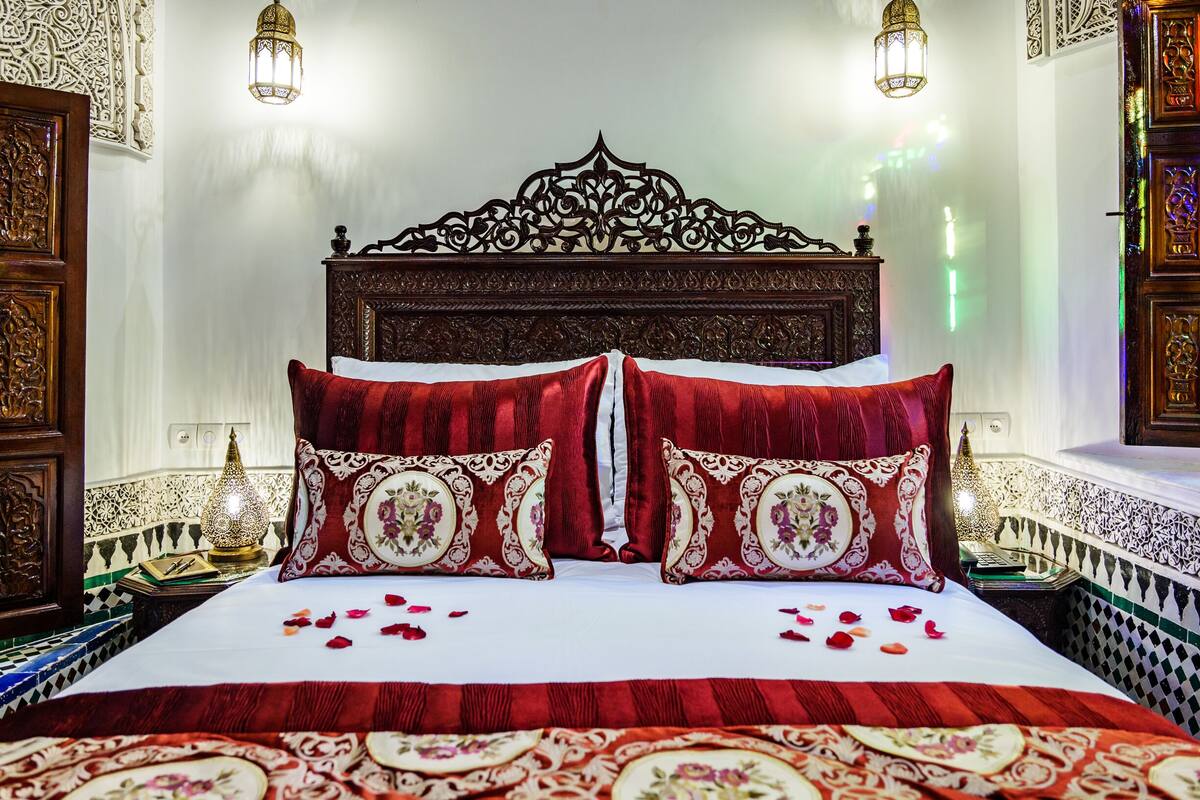 A bed with ornate headboard, red bedding, and decorative pillows.