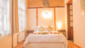 A bedroom with a large bed, a nightstand, a wall-mounted lamp, and a window with sheer curtains.
