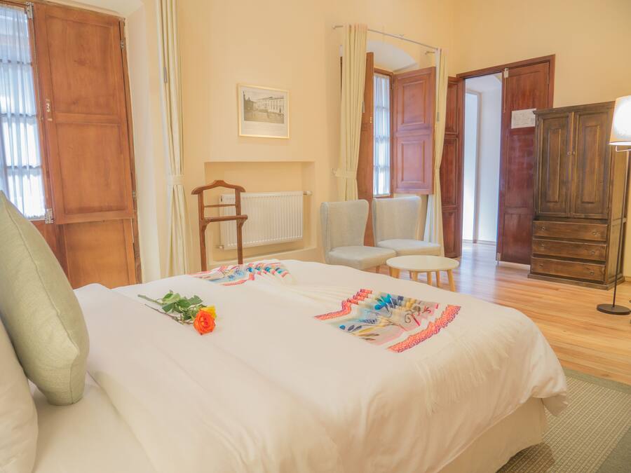 Habitación de hotel con cama, dos sillas, una mesita, un radiador y un armario.