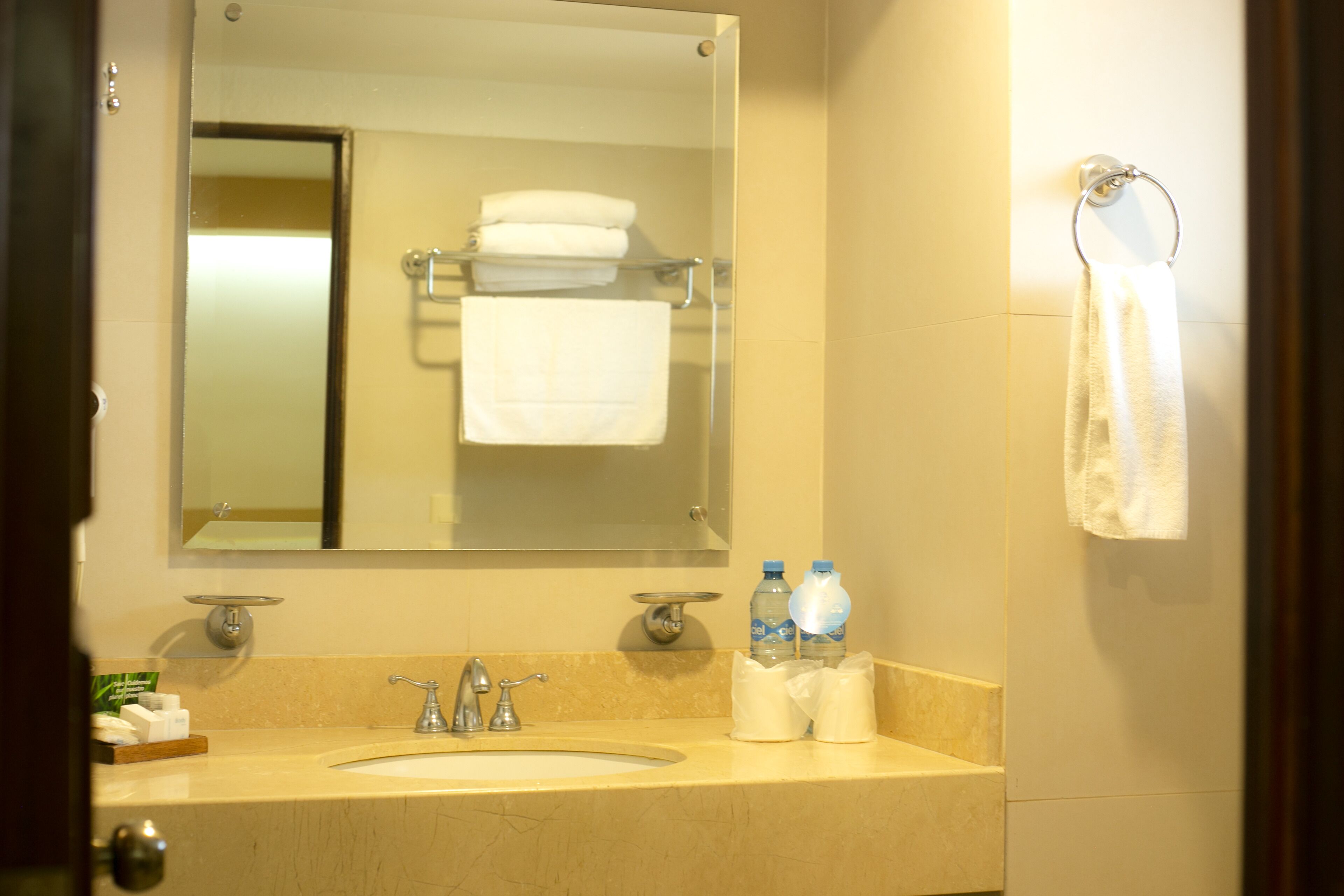 A bathroom with a sink, mirror, towel rack, and two bottles of water.