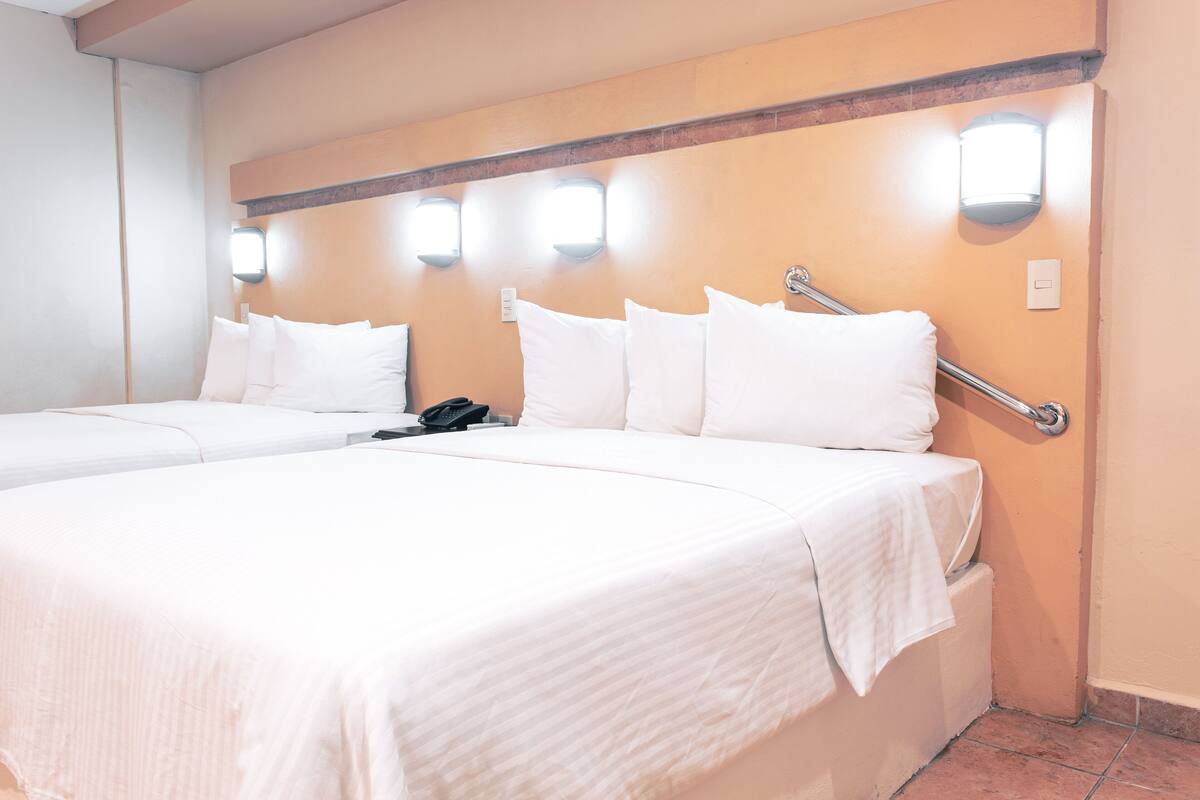 A hotel room with two beds, a bedside table, a phone, and wall-mounted lights.