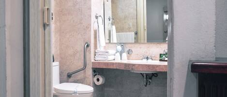 A bathroom with a toilet, sink, mirror, and towel rack.