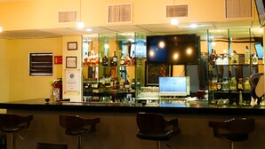A bar with a glass partition, shelves of liquor bottles, a television, and bar stools.