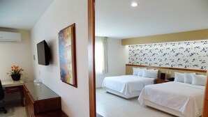 A hotel room with two beds, a desk, a chair, a TV, and a floral-patterned wall.