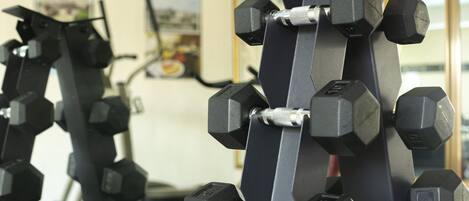 Una hilera de mancuernas hexagonales en un estante dentro de un gimnasio.