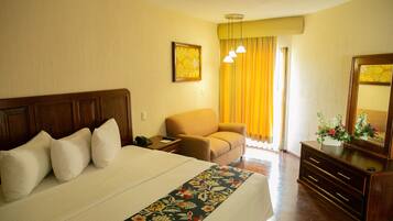Habitación de hotel con una cama grande, una mesita de noche de madera, una silla, un aparador y un espejo.