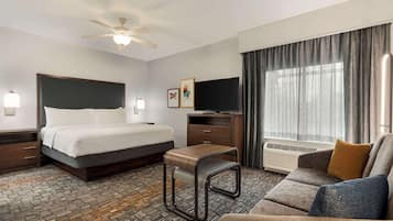 A hotel room with a bed, a sofa, a desk, a TV, and a ceiling fan.