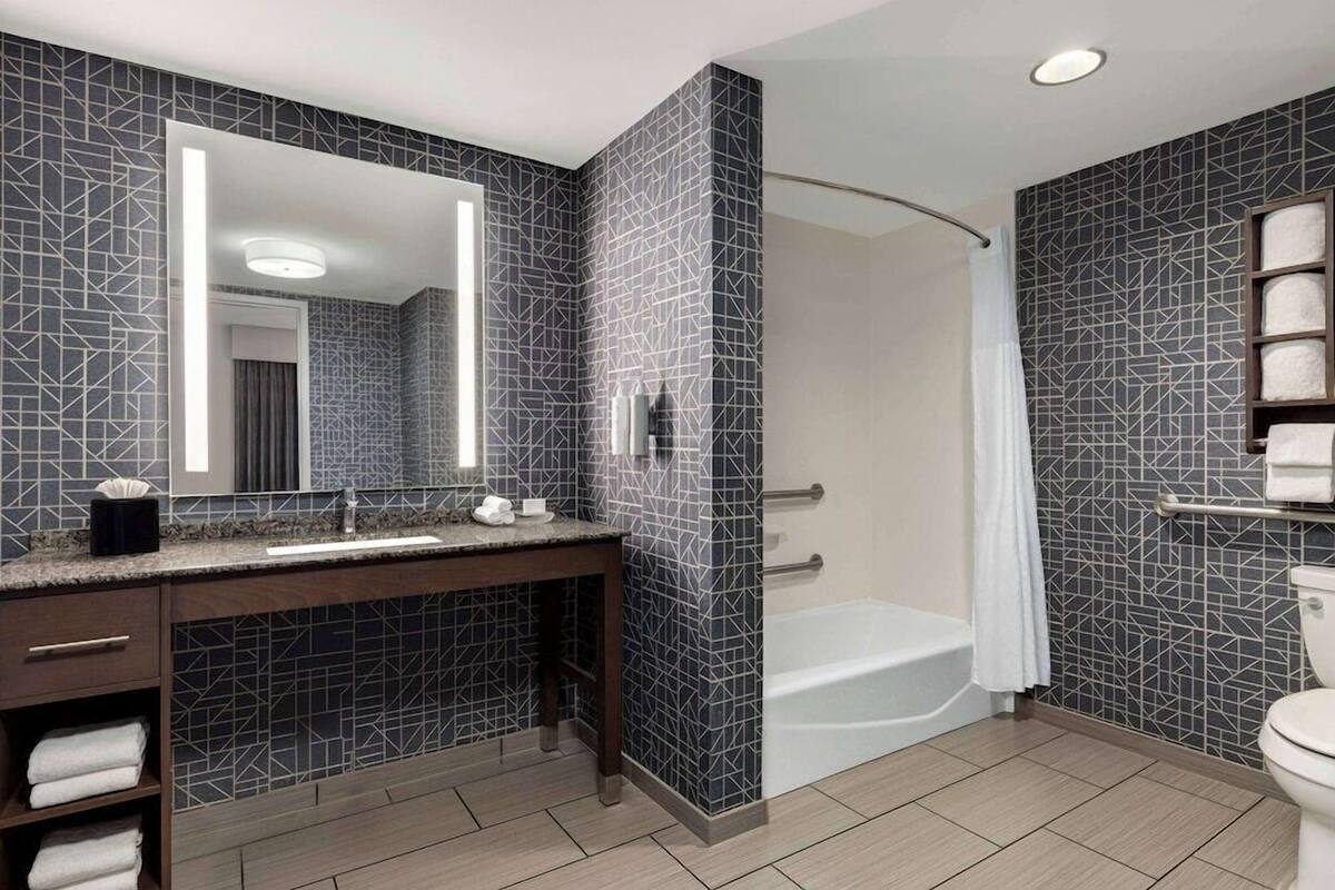 A modern bathroom with a dark patterned wall, a vanity with a mirror, a bathtub, and a toilet.