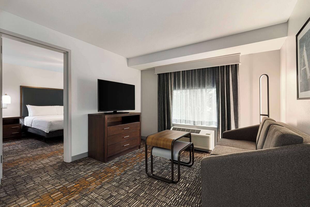 A hotel room with a bed, a TV, a desk, a chair, and a sofa.