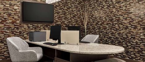 A modern conference room with a large flat-screen TV, a round table, and two office chairs.