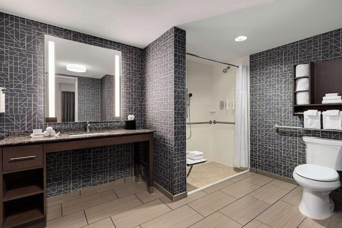 Une salle de bain moderne avec un grand miroir, des carreaux à motifs foncés, une douche et des toilettes.