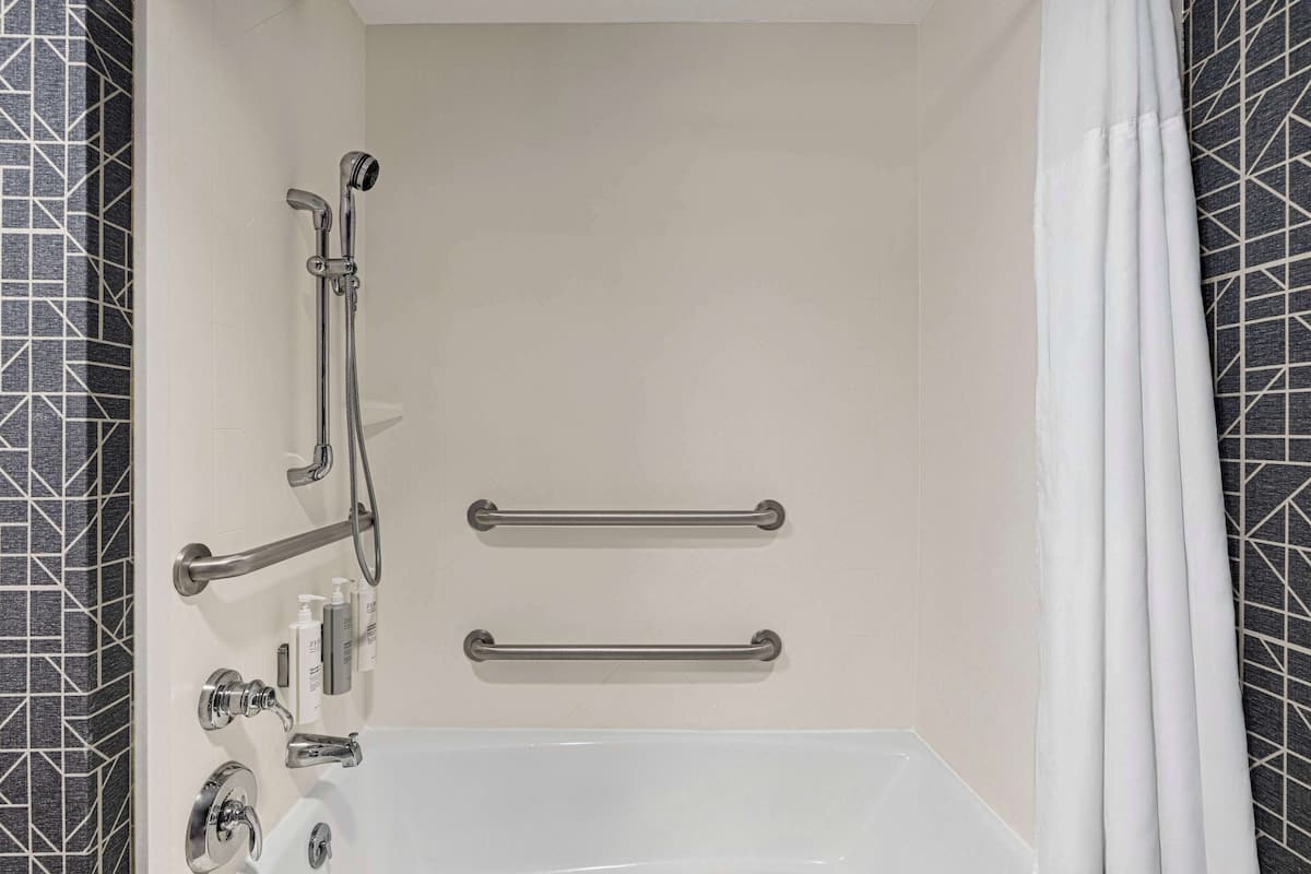 A bathroom with a bathtub, grab bars, and a showerhead.